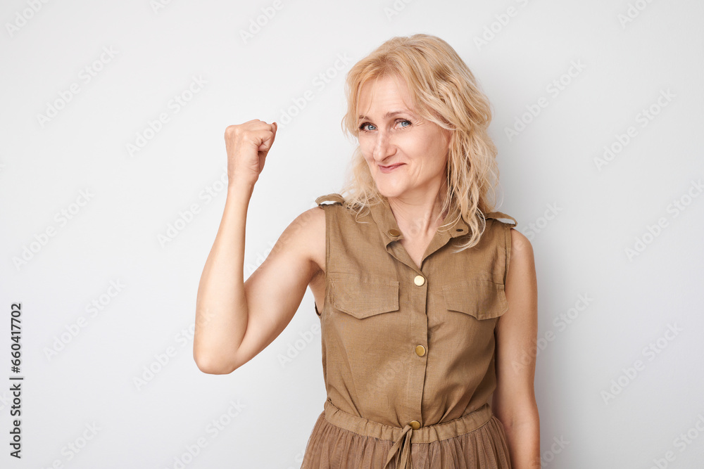Portrait of confident 50 year old woman showing biceps, demonstrating strength isolated on white studio background. Lucky winner concept Portrait of confident 50 year old woman showing biceps, demonstrating strength isolated on white studio background. Lucky winner concept