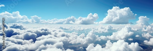 A panoramic background image for creative content, capturing a vast expanse of fluffy clouds hovering near the horizon against a serene blue sky. Photorealistic illustration © DIMENSIONS