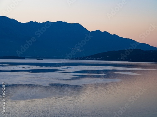 a blue lake at sunset with mountains in the distance and a boat out to sea 