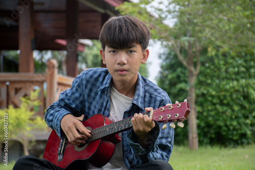 Asian cute boy playing guitar in the front yard of his own house happily, soft focus, concept for recreational activity and free times hobbies of children around the world.