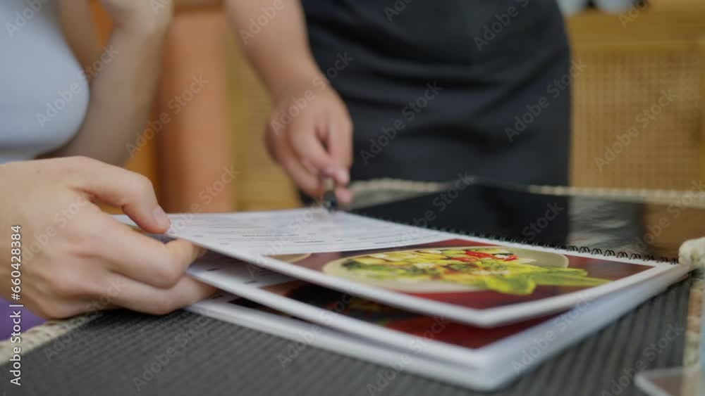Female hands holding menu in cafe turning pages, choosing food and drinks, the waitress helps to choose a dish, shows the woman what she is looking for. Female hands holding menu in cafe turning pages, choosing food and drinks, the waitress helps to choose a dish, shows the woman what she is looking for.