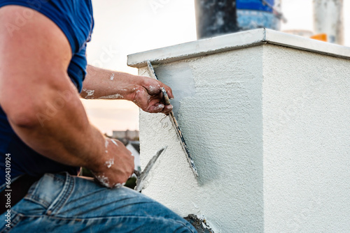 Obraz na płótnie Worker applying white seamless concrete pebble-dash plaster on chimney using putty knife