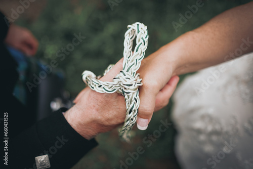 Close up picture of bride and groom's hands tied with white and green rope.