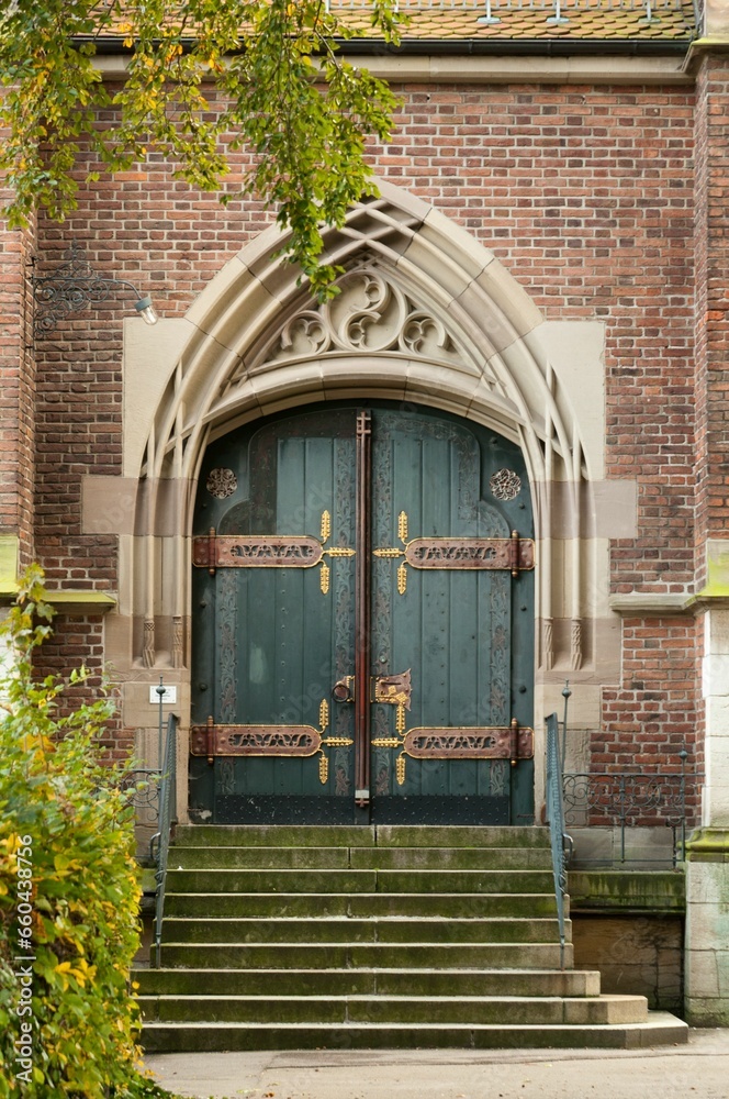 Brick building with two green doors featuring detailed and ornate designs Brick building with two green doors featuring detailed and ornate designs