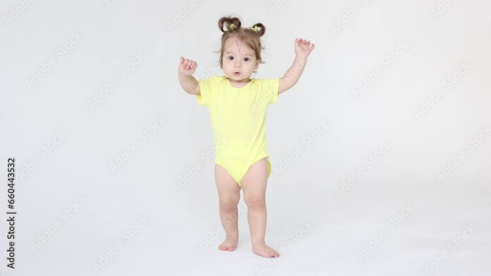 cute baby girl in a yellow bodysuit takes her first steps on a white background cute baby girl in a yellow bodysuit takes her first steps on a white background