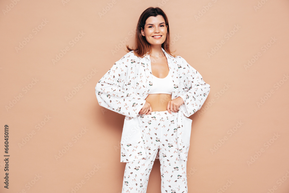 Obraz premium Young beautiful smiling female in trendy summer costume clothes. Carefree woman posing near beige wall in studio. Positive model having fun indoors. Cheerful and happy