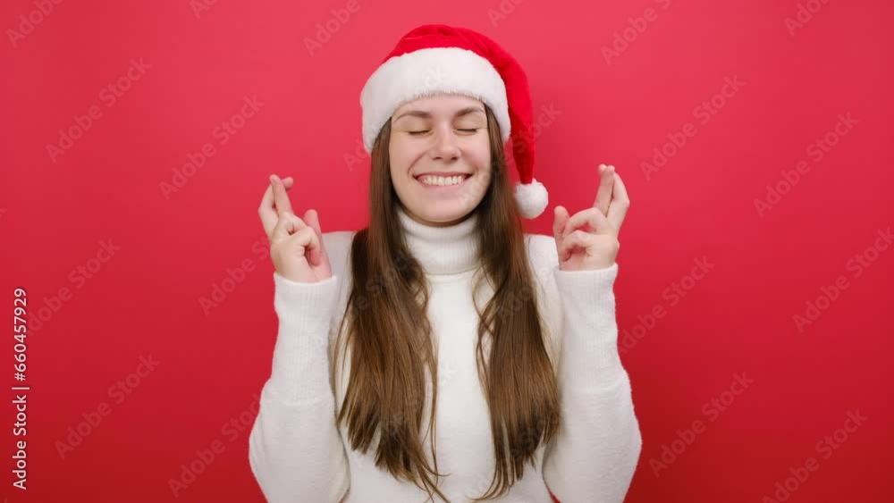 Pretty young woman wears warm sweater and Xmas Santa hat wait for special moment keep fingers crossed look aside, posing isolated over pastel red background. Happy New Year 2024 celebration concept Pretty young woman wears warm sweater and Xmas Santa hat wait for special moment keep fingers crossed look aside, posing isolated over pastel red background. Happy New Year 2024 celebration concept