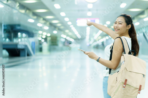Happy beautiful Asian solo female tourist walking in the airport terminal, woman walking and talking with her friend on mobile phone. Asian woman passenger walks in airport terminal to departure gate.