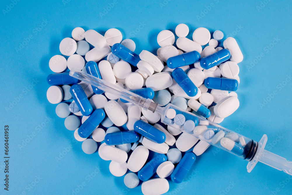 Pills in the shape of a heart and a syringe on a blue background. Pills for heart health. The concept of medicine and health care Pills in the shape of a heart and a syringe on a blue background. Pills for heart health. The concept of medicine and health care