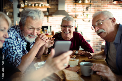 Group of senior friends using a smartphone while having breakfast together in the kitchen