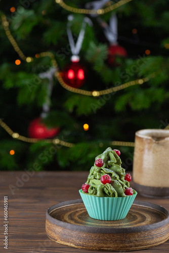 Green cupcake with cranberries on the background of the Christmas tree. Vegan, gluten, lactose, sugar free.