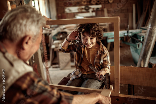 Senior male carpenter teaching his grandson how to use a hammer in a carpentry shop