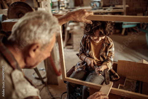 Senior male carpenter teaching his grandson how to use a hammer in a carpentry shop