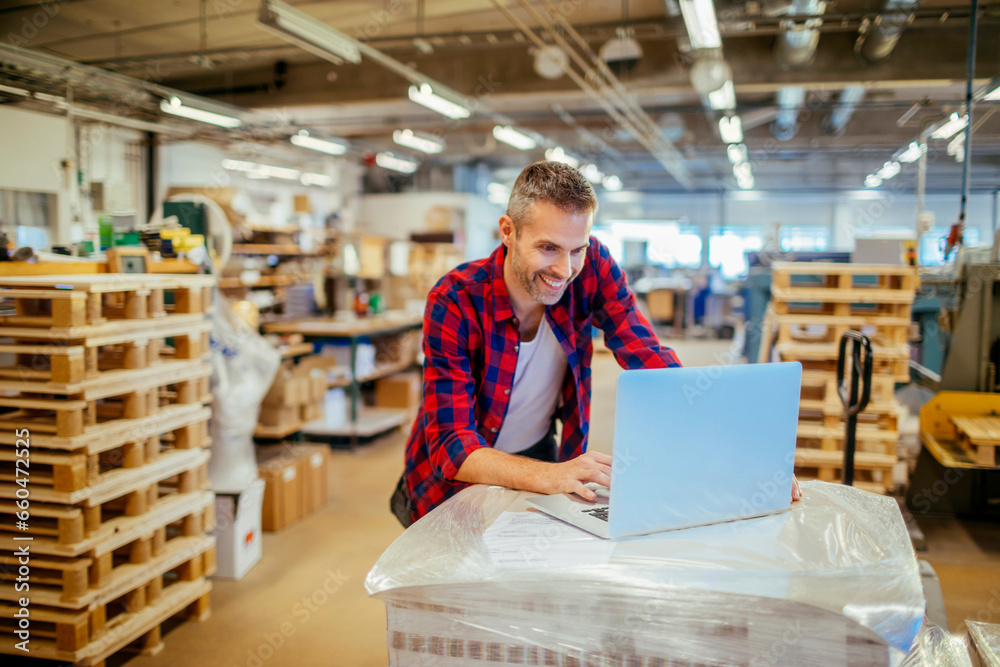 Fototapeta premium Young man using a laptop while working in a warehouse
