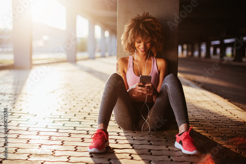 Fototapeta Naklejka Na Ścianę i Meble -  Young fit woman using a smartphone before jogging under a bridge in the city