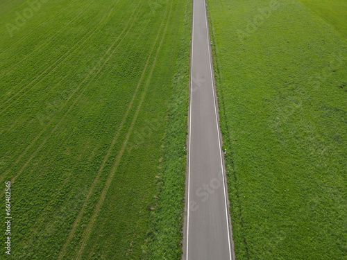 View from above of a straight road between green grass fields in the landscape 