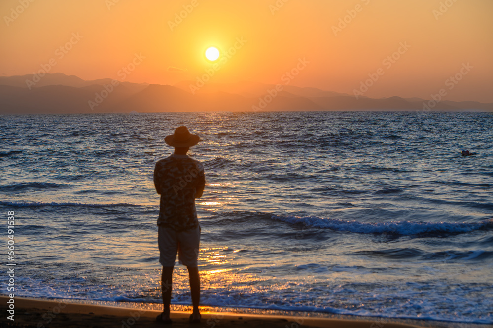 handsome young man in a hat looks into the sea at a Mediterranean sunset