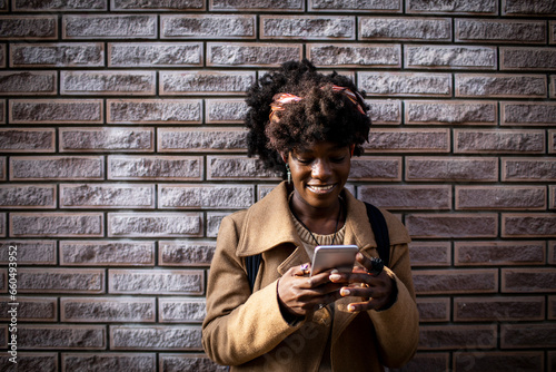 Portrait of a young African American woman using a smartphone with a brick wall background photo