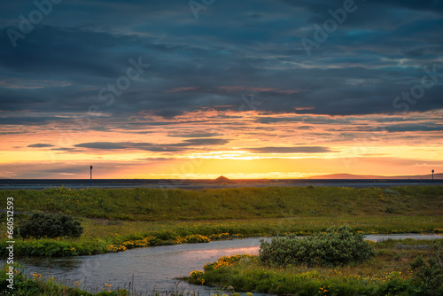 Rural scene of sunset over meadow with stream in summer