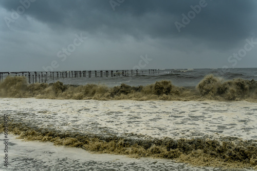Rough see with violent waves with a broken pier on the background. Harsh storm condition with muddy waves.