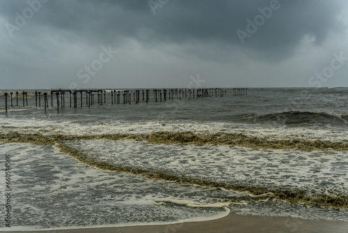 Rough see with violent waves with a broken pier on the background. Harsh storm condition with muddy waves.