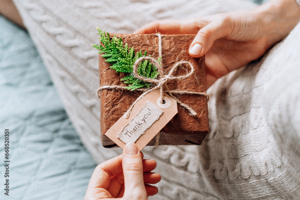 Fototapeta premium Female hands holding gift handcrafted box thoughtfully wrapped in eco-friendly packaging with tag with the words thank you. Sustainable and eco conscious living concept.