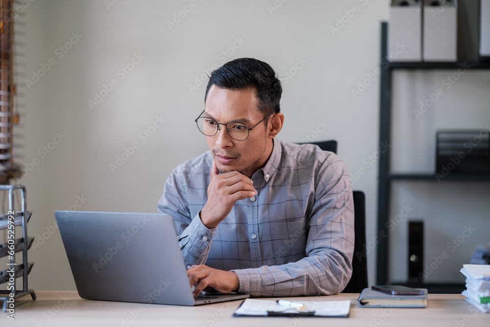 Portrait of young asian businessman, man smiling while sitting inside office, boss in business suit at workplace using laptop. Portrait of young asian businessman, man smiling while sitting inside office, boss in business suit at workplace using laptop.