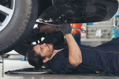 Male car mechanic worker working and repair, maintenance underneath lifted car. Mechanic vehicle service checking under car in garage. Auto car repair service, maintenance concept photo