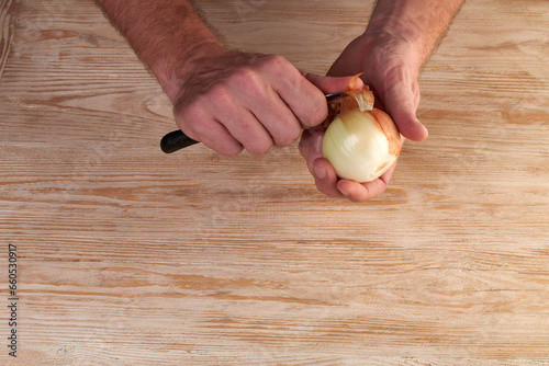 Men's hands are peels fresh onion with knife