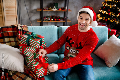 Photo of cheerful handsome young man sitting comfy sofa untie ribbon box unpack desirable giftbox christmastime house indoors