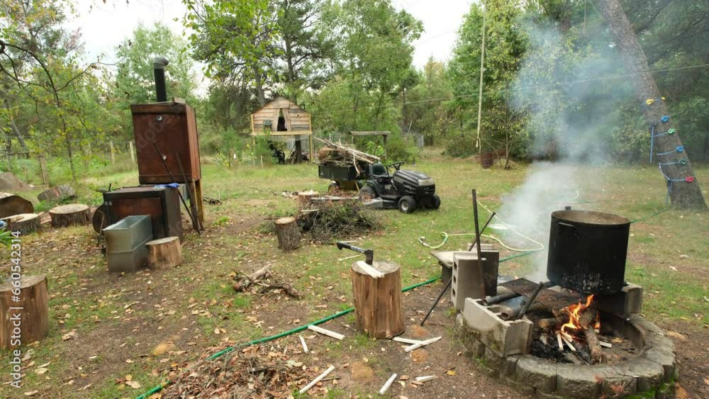 Suburban backyard while smoke rise from burning wood in the fire pit, home made smoker made from tool box on the left and tree house in the background. Suburban backyard while smoke rise from burning wood in the fire pit, home made smoker made from tool box on the left and tree house in the background.