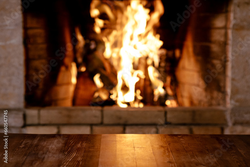 Empty old wooden table against burning wood in the fireplace