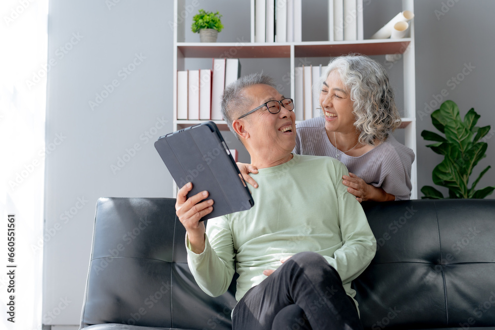 Happy mature couple using tablet at home. Happy elderly Asian couple laughing bonding together sitting at home table with tablet.