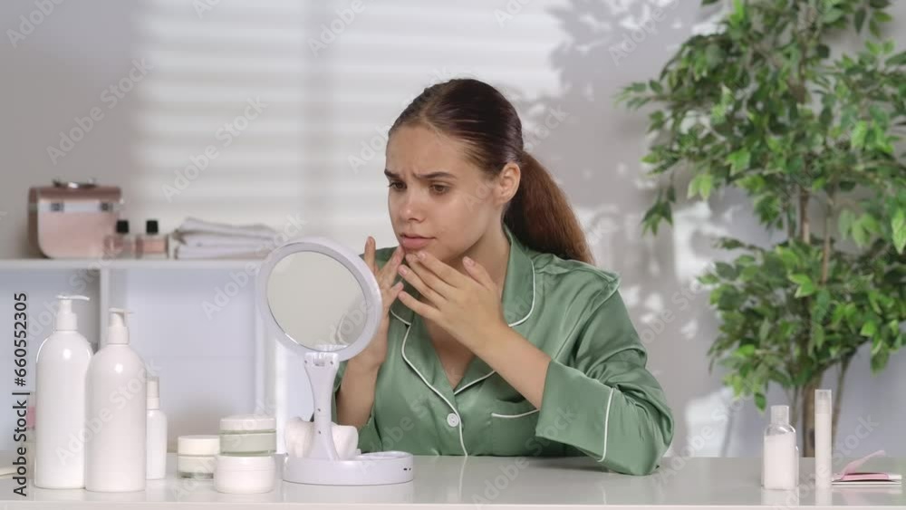 A pretty woman without makeup sits in front of a mirror at a dressing table. The woman smiles at her reflection until she notices a puffiness, swelling or pimple on her chin. Problematic facial skin. A pretty woman without makeup sits in front of a mirror at a dressing table. The woman smiles at her reflection until she notices a puffiness, swelling or pimple on her chin. Problematic facial skin.