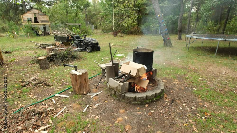 Suburban backyard while smoke rise from burning wood in the fire pit, lawnmower and trampoline and tree house in the background. Suburban backyard while smoke rise from burning wood in the fire pit, lawnmower and trampoline and tree house in the background.