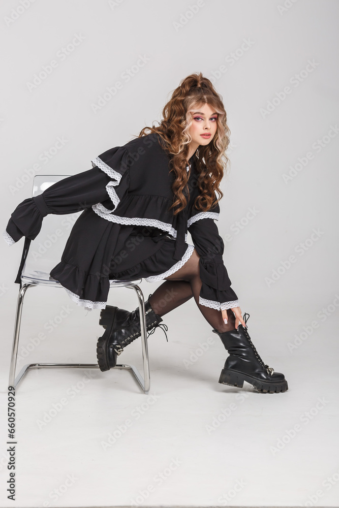 Fototapeta premium young girl in black school dress poses as doll on white background in studio