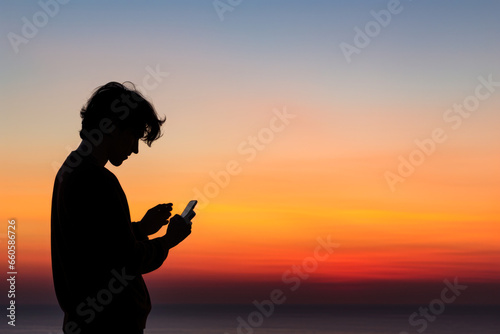 Vibrant sunset colors framing silhouetted man with smartphone