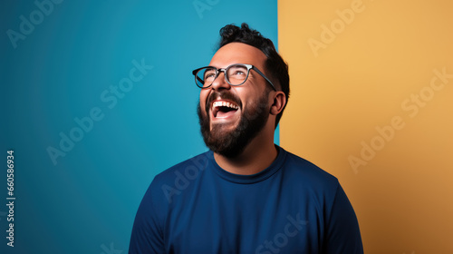 Young man laughs against a blue background.