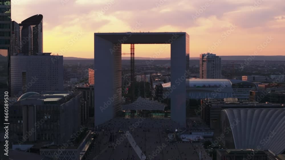 Aerial view of iconic Grande Arche de la Defense against colorful sunset sky. People admiring modern architecture in business district. Paris, France