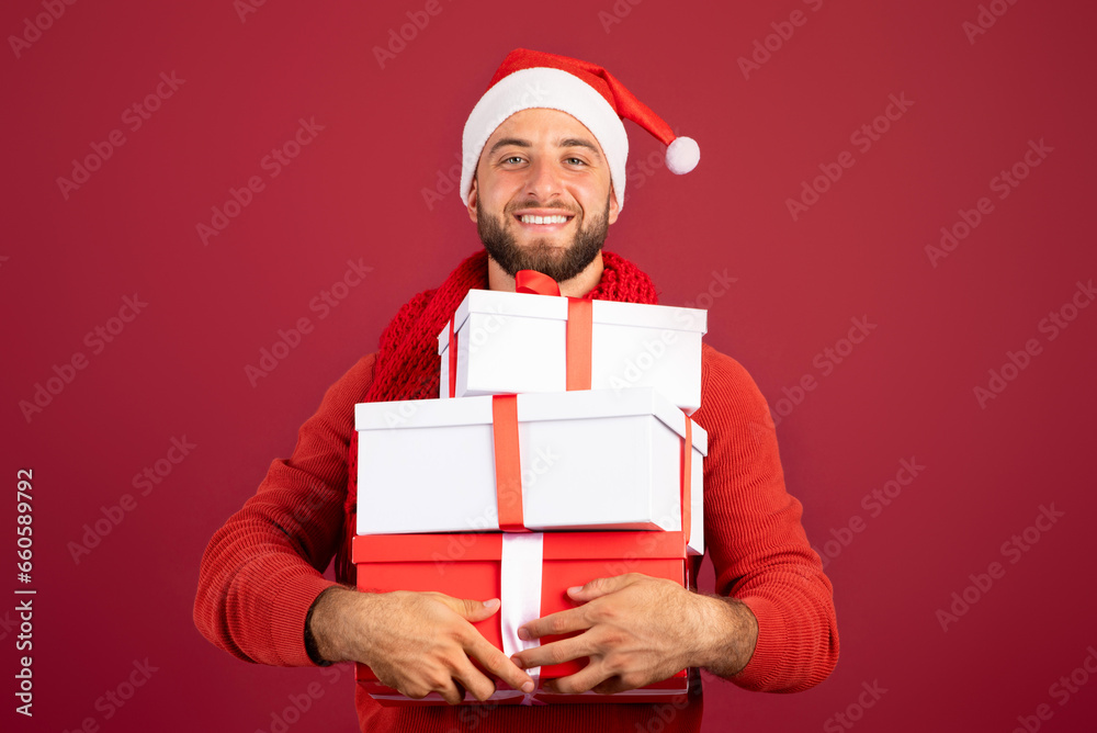 Cheerful handsome millennial caucasian man in Santa hat hold boxes of gifts, enjoy holidays