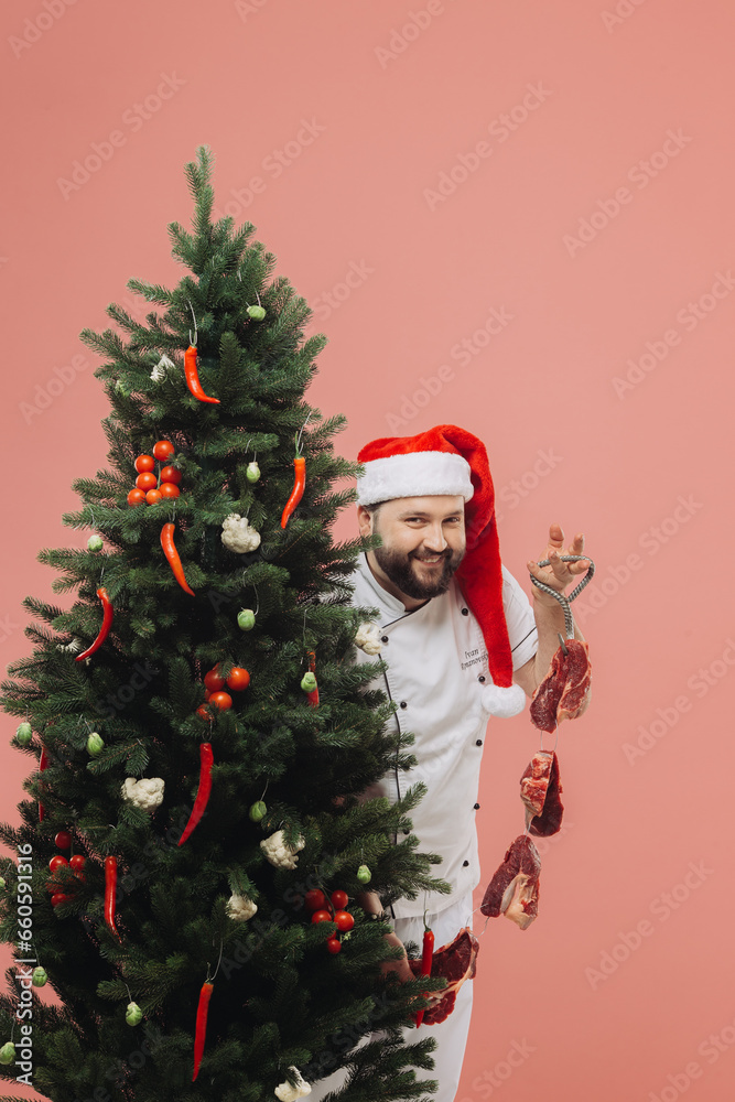 The concept of cooking and Christmas holidays. A chef in a Santa hat on the background of a Christmas tree.
