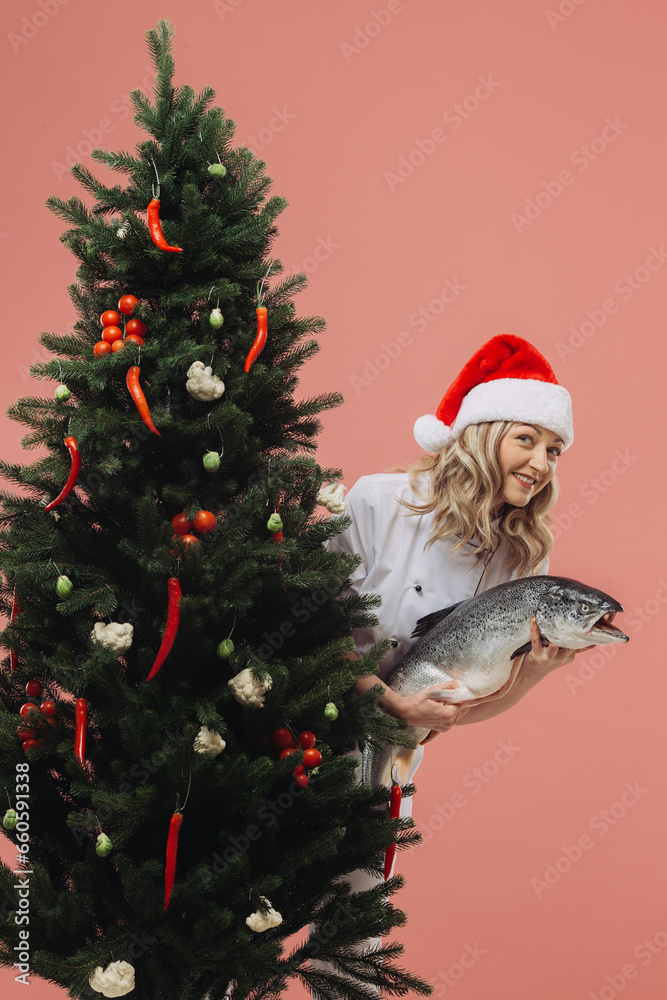 The concept of cooking and Christmas holidays. A beautiful woman cook holding a big fish in her hands, against the background of a Christmas tree. The concept of cooking and Christmas holidays. A beautiful woman cook holding a big fish in her hands, against the background of a Christmas tree.