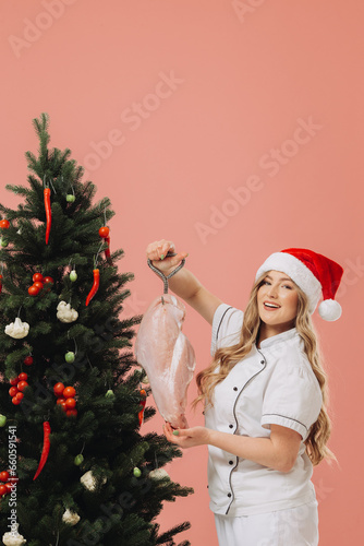 Concept of cooking and Christmas holidays. A beautiful blonde cook in a Santa hat poses against the background of a Christmas tree.