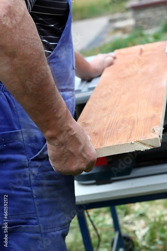 Worker with electric circular saw. Senior carpenter cuts wood, focus on saw, previously injured fingers can be seen.