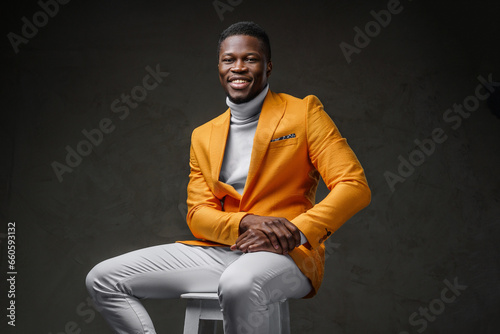 Foto A well-dressed cheerful dark-skinned man wearing a yellow jacket poses sitting o
