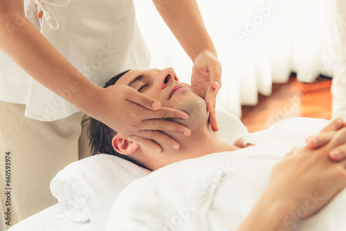 Caucasian man enjoying relaxing anti-stress head massage and pampering facial beauty skin recreation leisure in dayspa modern light ambient at luxury resort or hotel spa salon. Quiescent