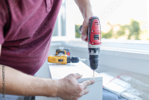Man worker assembling kitchen wooden elements with cordless drill.