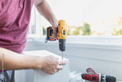 Man worker assembling kitchen wooden elements with cordless screwdriver