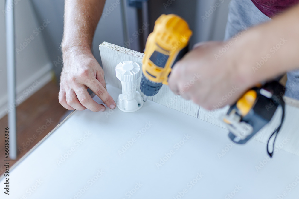Carpenter using electric cordless screwdriver for kitchen elements installation Carpenter using electric cordless screwdriver for kitchen elements installation
