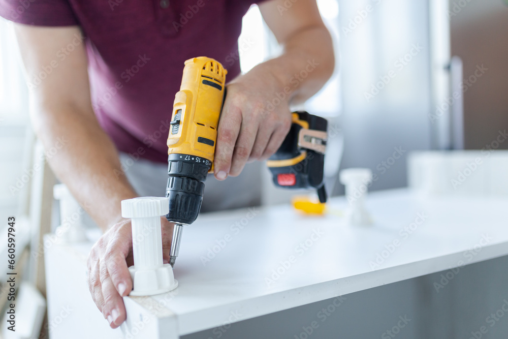 Carpenter using electric cordless screwdriver for kitchen elements installation